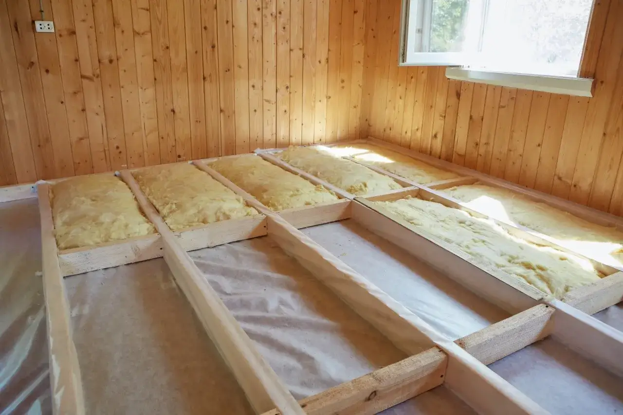 Golvbj&auml;lkar med isolering p&aring; plats f&ouml;r att isolera lekstuga. Tr&auml;v&auml;ggar och ett f&ouml;nster syns.