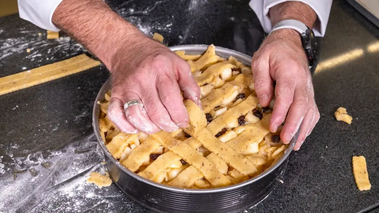 H&auml;nde legen das Gitter f&uuml;r ein Apfelkuchen-Rezept auf die F&uuml;llung.