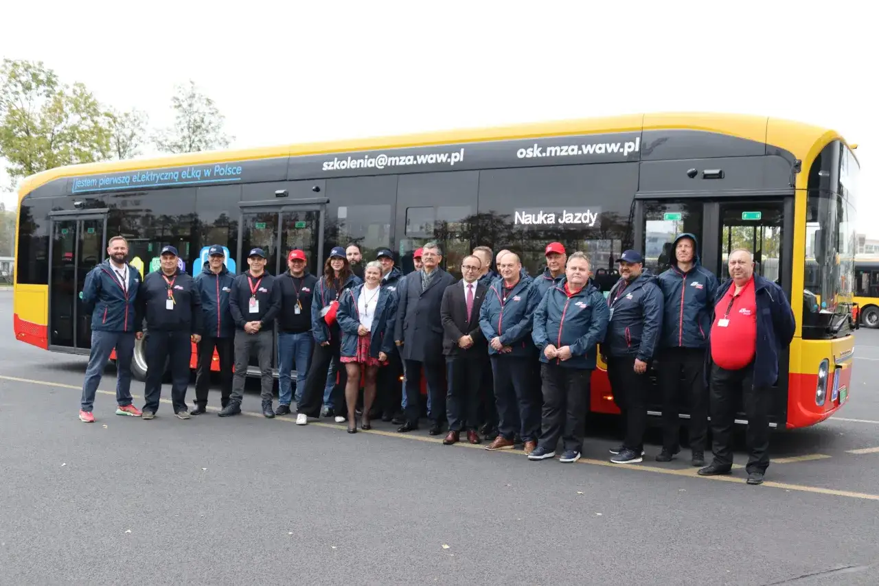 Grupa osób pozuje przed nowym autobusem elektrycznym. Na boku pojazdu widnieje napis