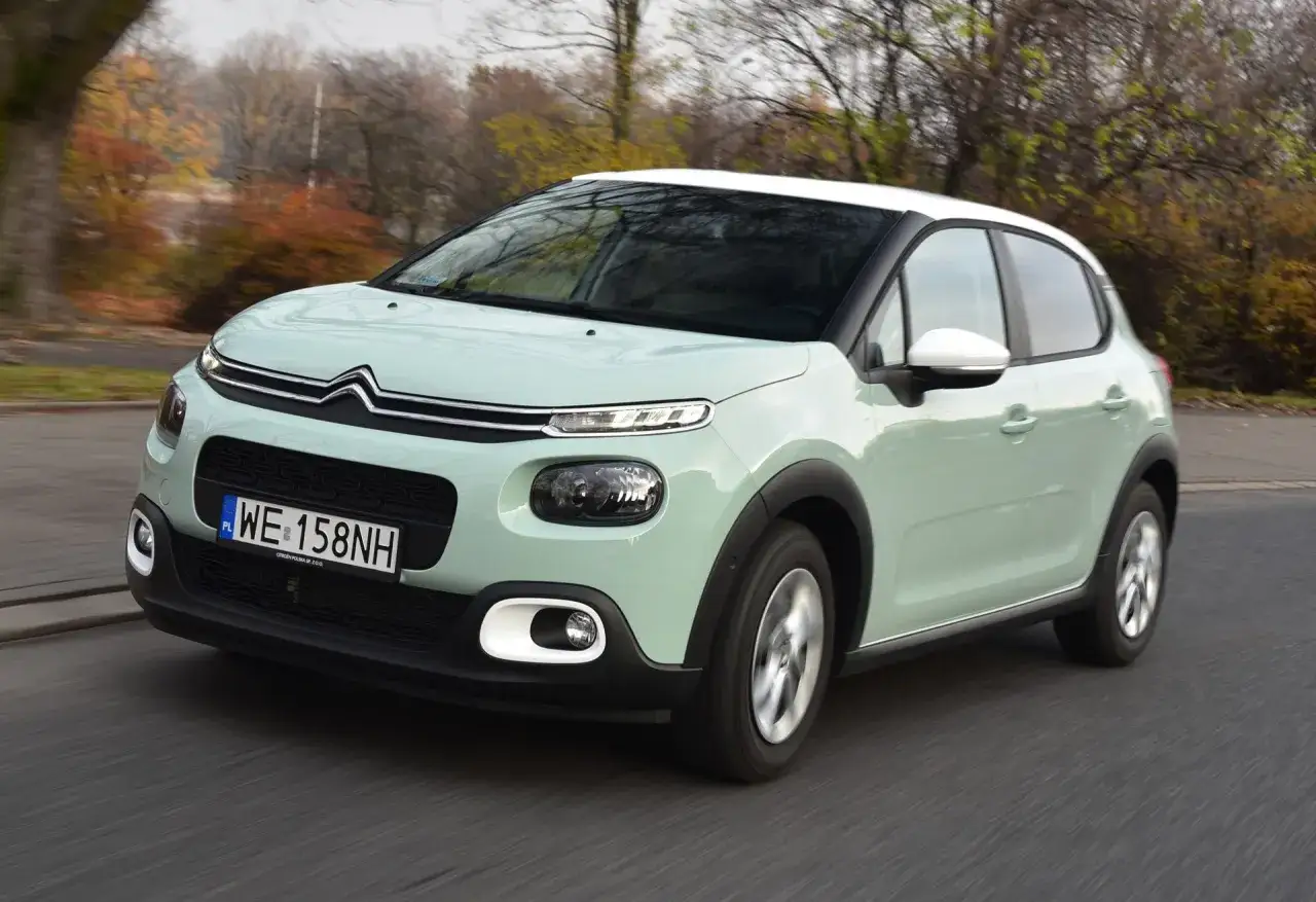 Jasnozielony Citroën C3 z białym dachem, idealne auto do 40 tys. zł, jedzie po drodze wśród jesiennych drzew.