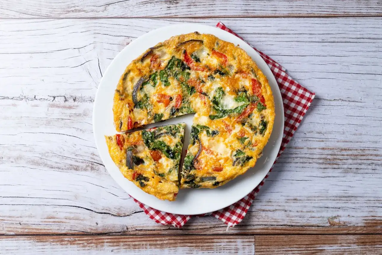 Frittata con verdure, cotta in friggitrice ad aria, servita su un piatto bianco con tovagliolo a quadri rossi.