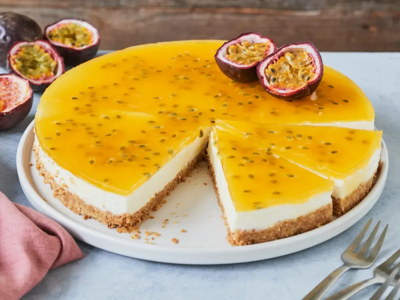 Ein cremiger Maracuja Cheesecake mit fruchtiger Passionsfruchtsauce und knusprigem Boden. Zwei Stücke sind bereits angeschnitten.