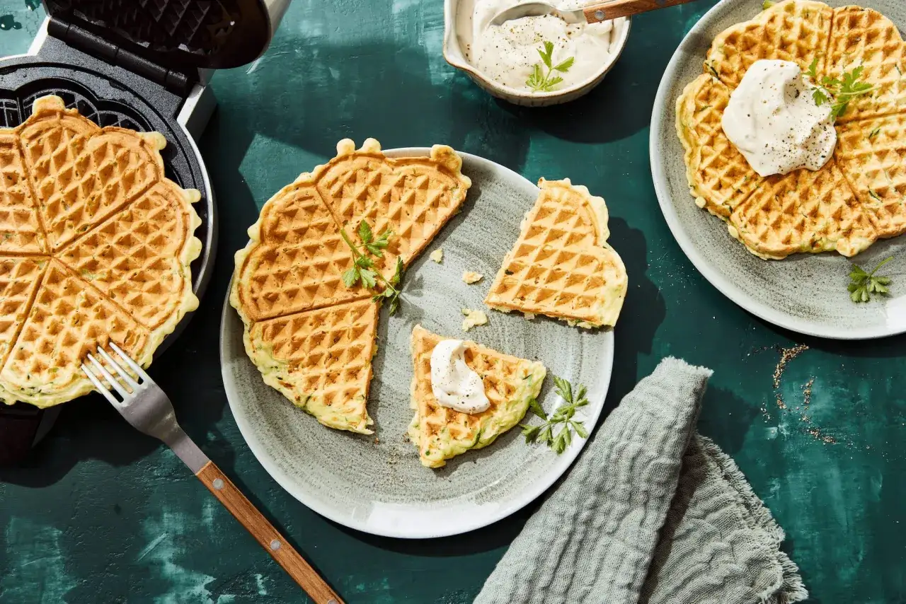 Herzhafte zucchini waffeln, frisch aus dem Waffeleisen, mit einem Klecks Dip und Petersilie garniert.