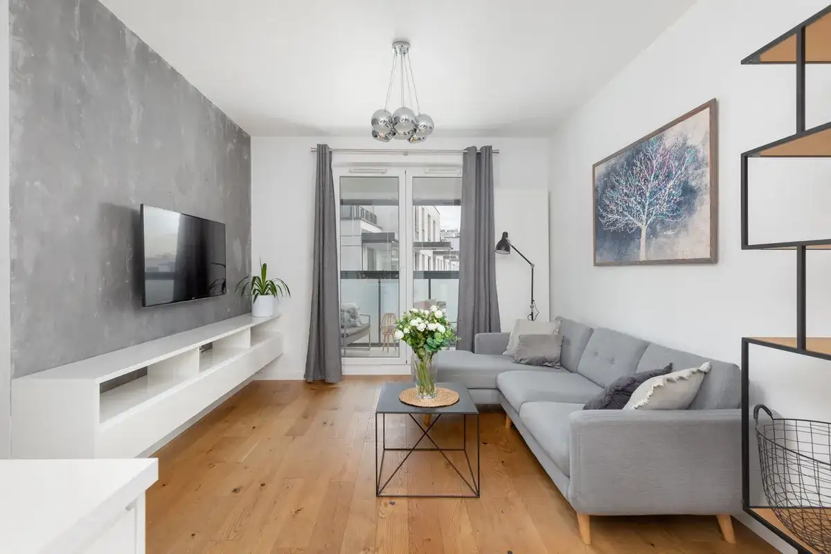 Nowoczesne wykończenie mieszkań Warszawa: szara sofa, betonowa ściana, drewniana podłoga i sztuka.