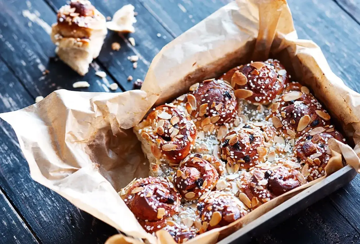 En form med nybakade, gyllene snabba butterkakor toppade med mandel och p&auml;rlsocker. En ensam bulle ligger bredvid.