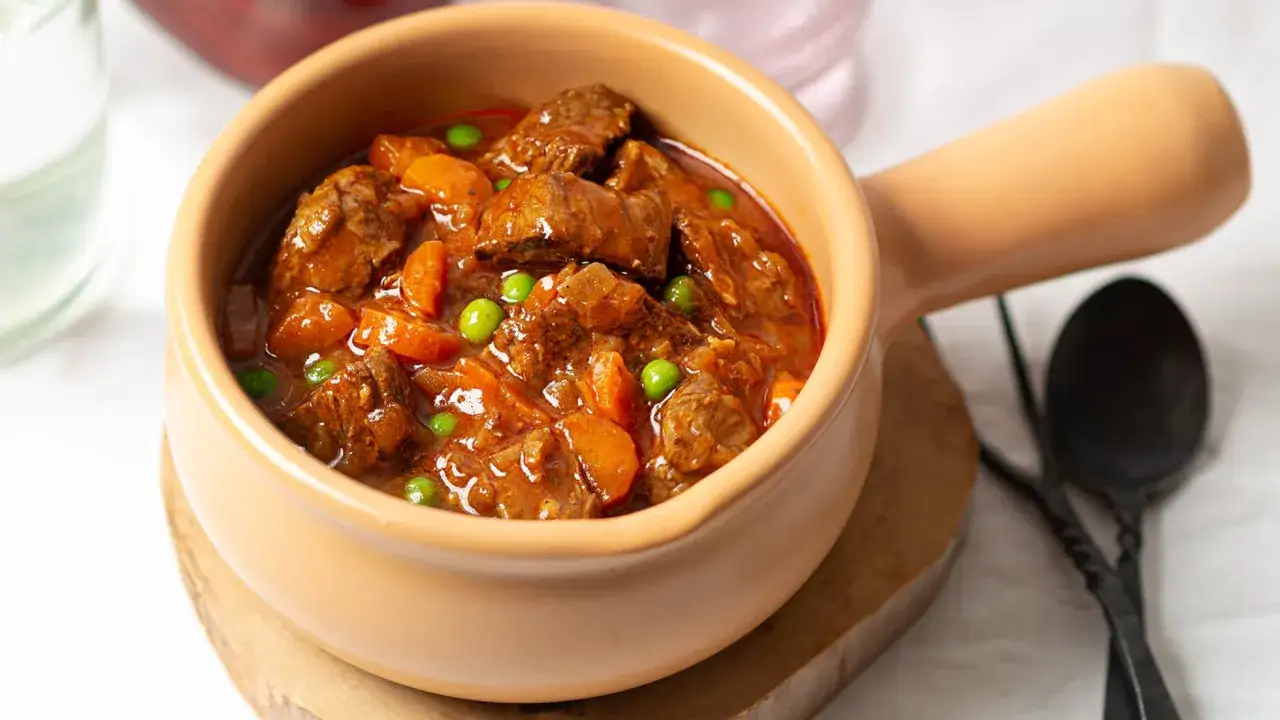 Ternera a la jardinera en cazuela de barro, con trozos de carne tierna, zanahorias y guisantes en una rica salsa.