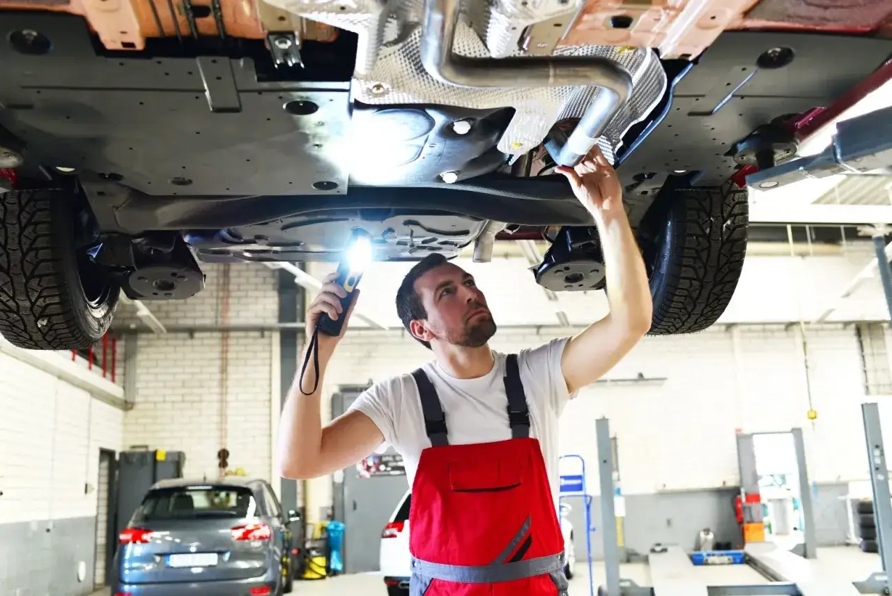 Mechanik z latarką sprawdza podwozie samochodu, wykonując naprawę układu wydechowego.