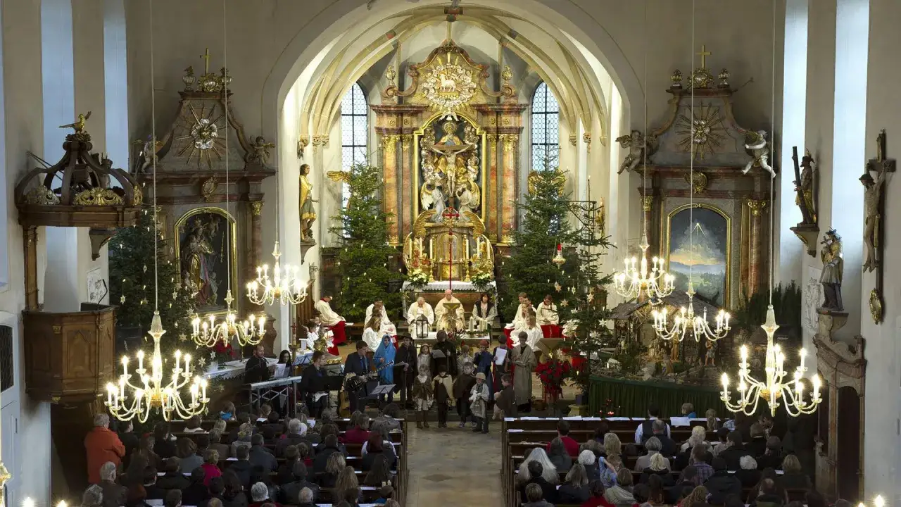 Festlicher Gottesdienst am Heiligen Abend in einer Kirche mit Krippe, Weihnachtsb&auml;umen und vielen Gl&auml;ubigen.
