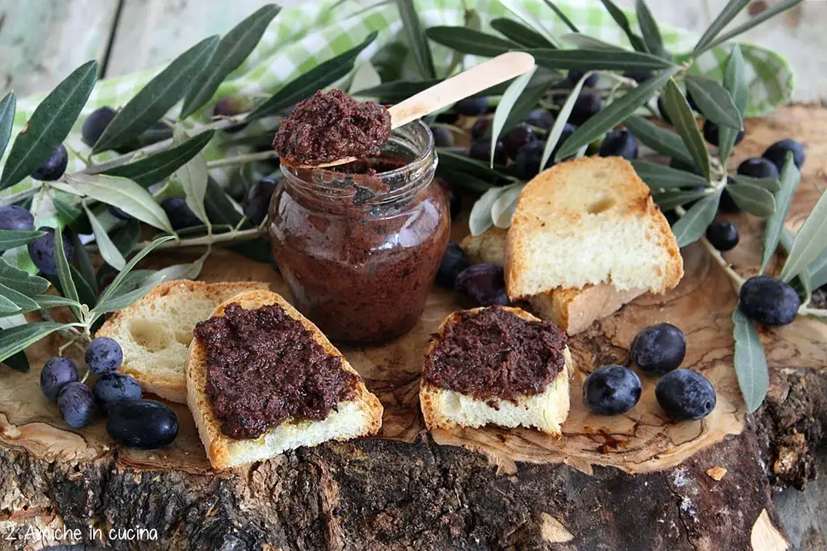 Bruschette con crema di olive, un vasetto pieno di sapore e rametti di ulivo fresco.
