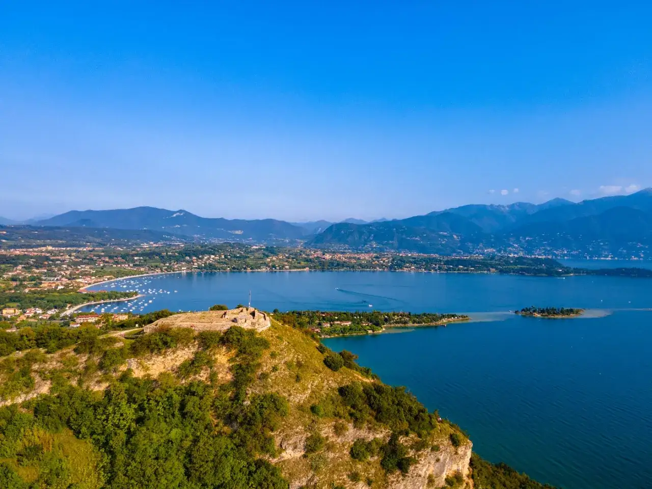 Rocca di Manerba domina il lago di Garda, con rovine antiche sulla cima di una collina verdeggiante e un panorama mozzafiato.