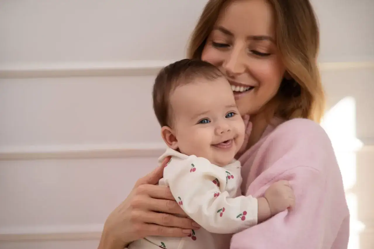 Uśmiechnięta mama tuli swoje radosne dziecko. To urocza sesja na roczek w domu, pełna miłości i beztroski.