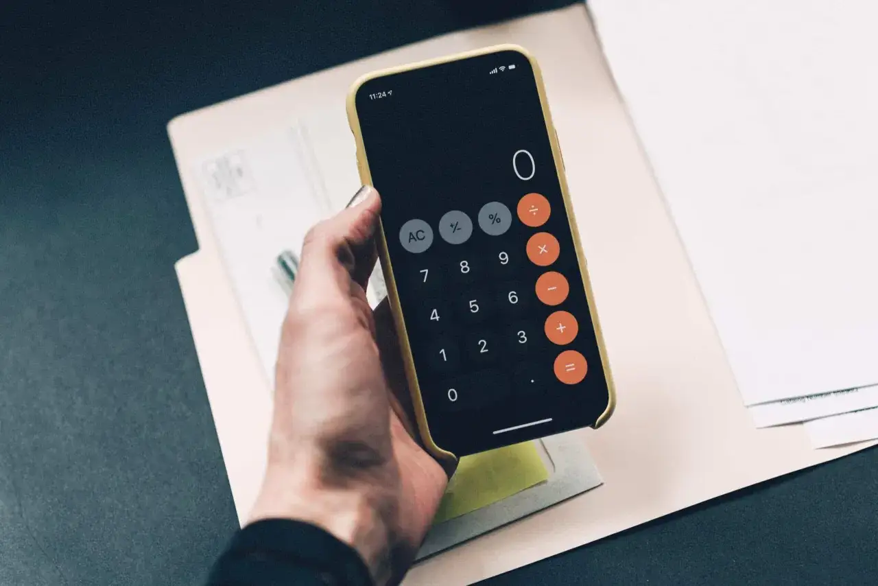 En hand h&aring;ller en guldf&auml;rgad mobil med en kalkylatorapp &ouml;ppen. Kanske f&ouml;r att budgetera f&ouml;r att renovera hus.