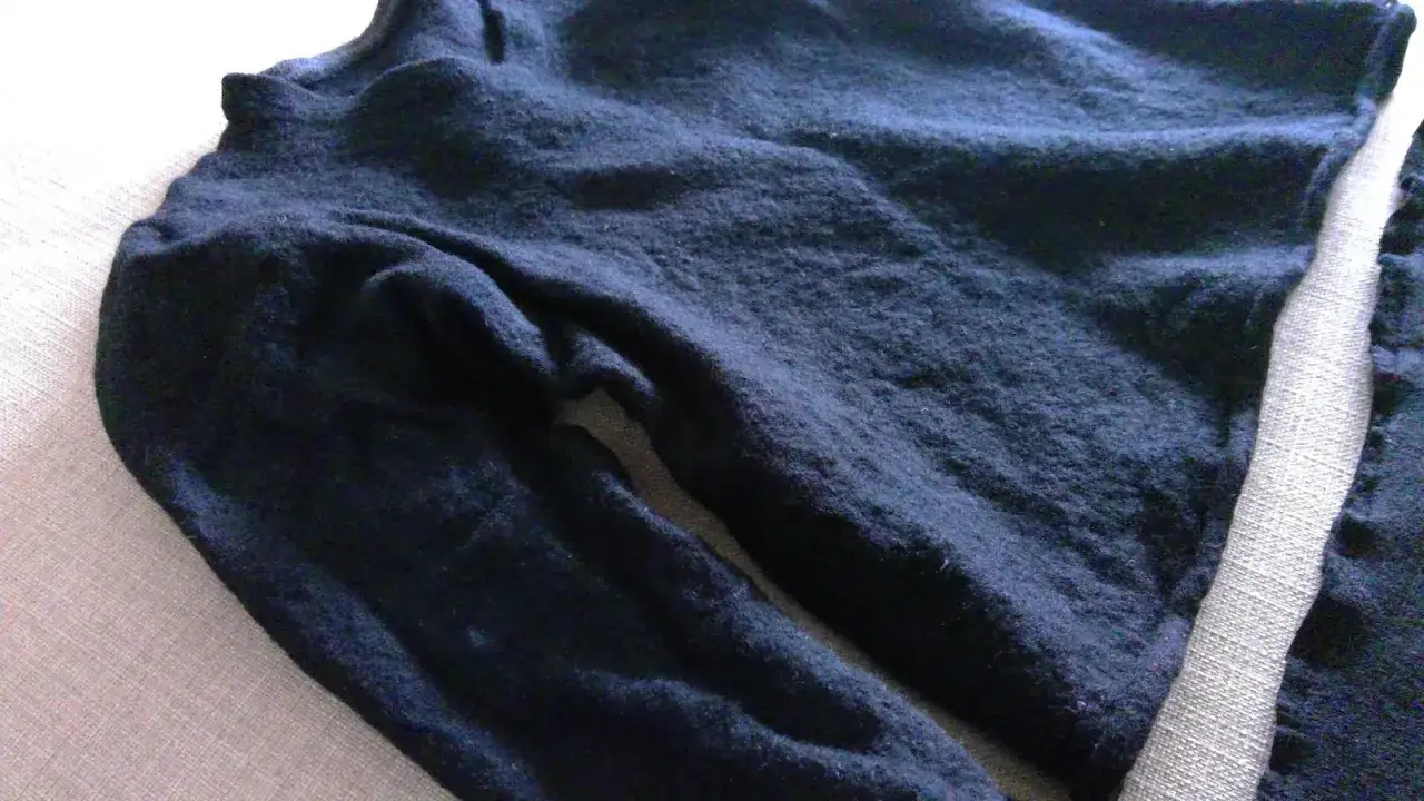 Ciemnogranatowy, sfilcowany sweter z długim rękawem, leżący na jasnym tle.