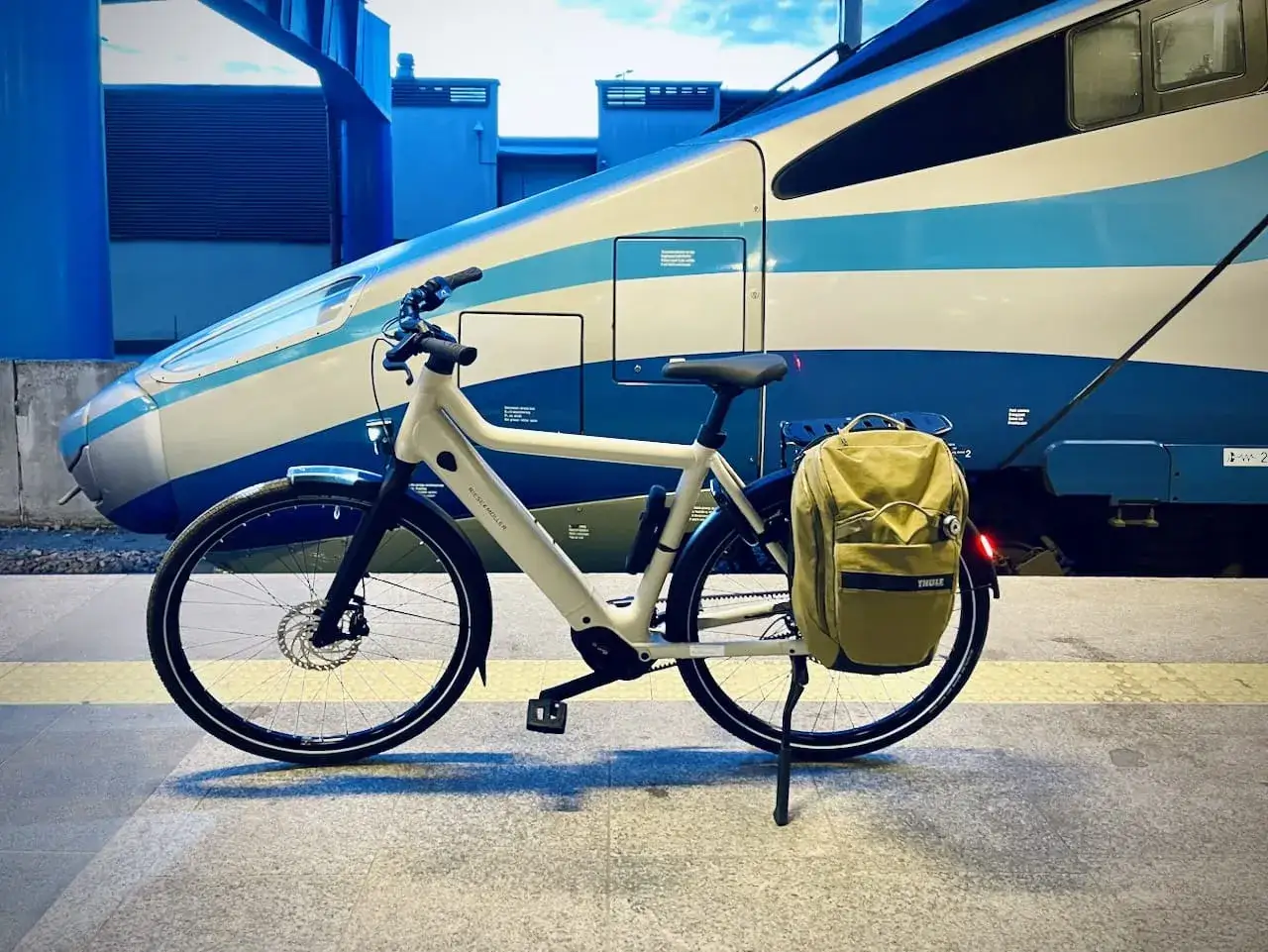 Biały rower z sakwą czeka na peronie obok pociągu Pendolino. Idealny towarzysz podróży, gdy chcesz połączyć jazdę rowerem z szybką koleją.