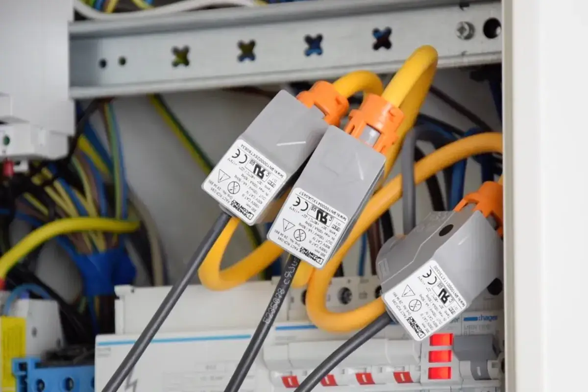 W rozdzielnicy elektrycznej widoczne są trzy cewki Rogowskiego z pomarańczowymi złączami, podłączone do żółtych przewodów.