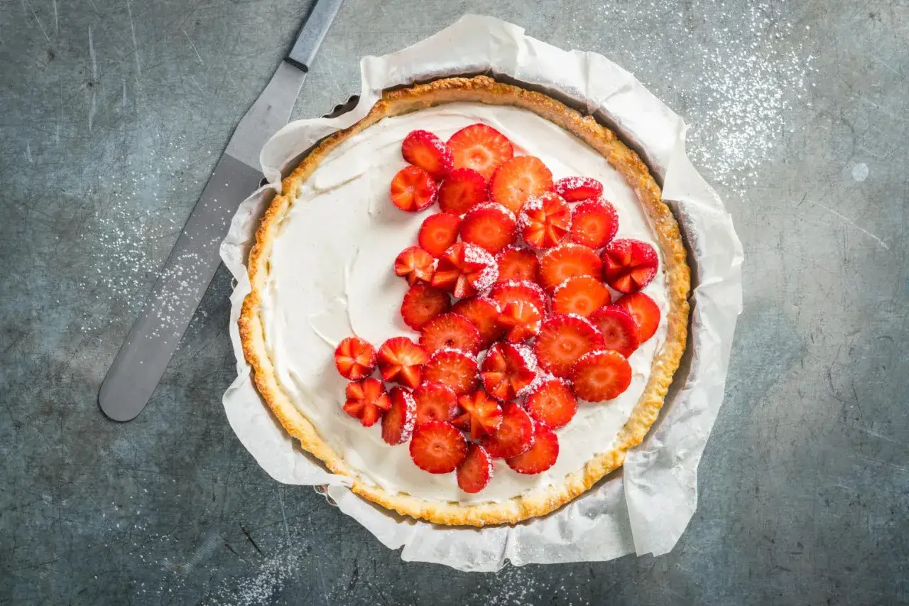 Tarte aux fraises mascarpone, garnie de fraises fraîches coupées et saupoudrée de sucre glace. Un délice prêt à être dégusté.