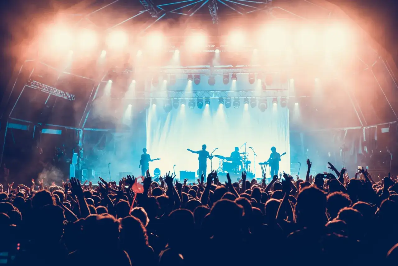 Eine Band spielt auf einer Bühne, während das Publikum jubelt. Die Lichter sind hell und die Stimmung ist elektrisierend. Man fragt sich: welche Konzerte sind heute?