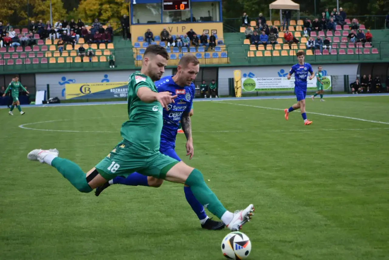 Piłkarz w zielonej koszulce z numerem 18 próbuje odebrać piłkę rywalowi. Emocje na boisku podczas meczu 3 liga grupa 4.