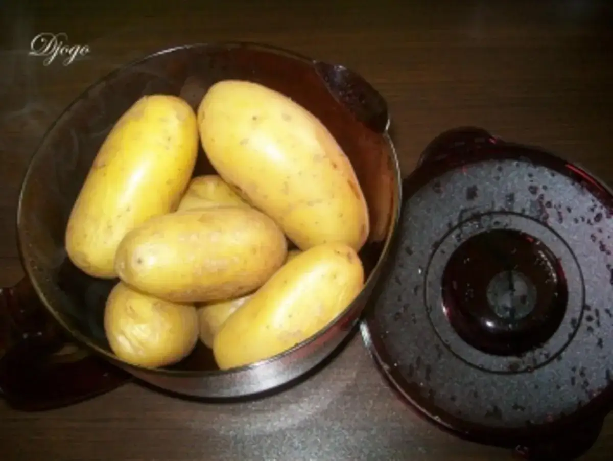 Frische Kartoffeln in einer Glassch&uuml;ssel, bereit f&uuml;r die Mikrowelle. Daneben liegt der Deckel eines Mikrowellen-Kochgeschirrs.