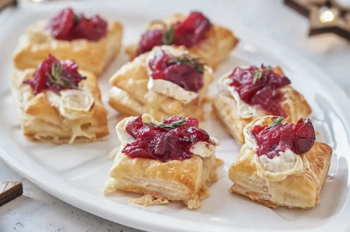 Kruche ciasto francuskie z roztopionym serkiem camembert i żurawiną, ozdobione gałązką rozmarynu.
