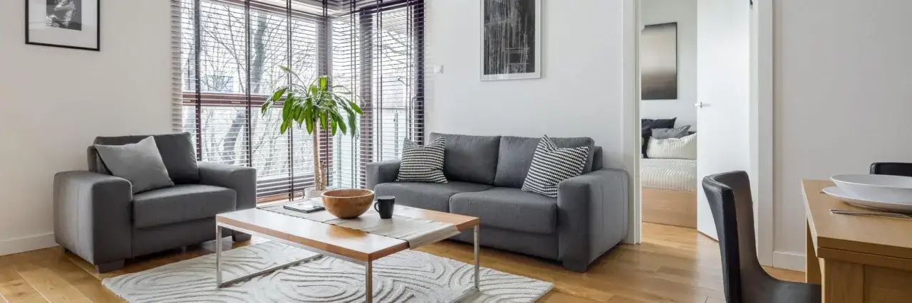 Salon moderne avec canapé gris, table basse en bois et tapis blanc. Le mobilier déductible frais notaire est bien mis en valeur.