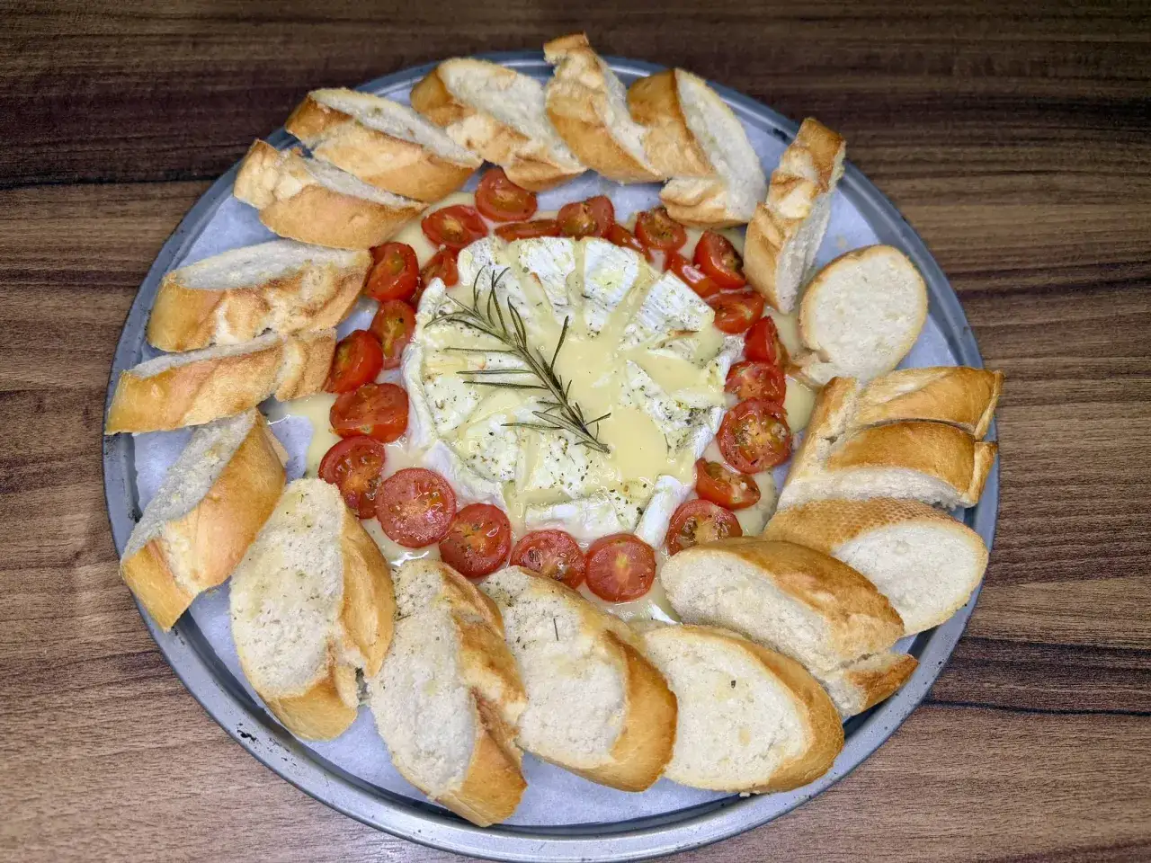Pyszny camembert z piekarnika, otoczony pieczywem i pomidorkami koktajlowymi, czeka na degustację.