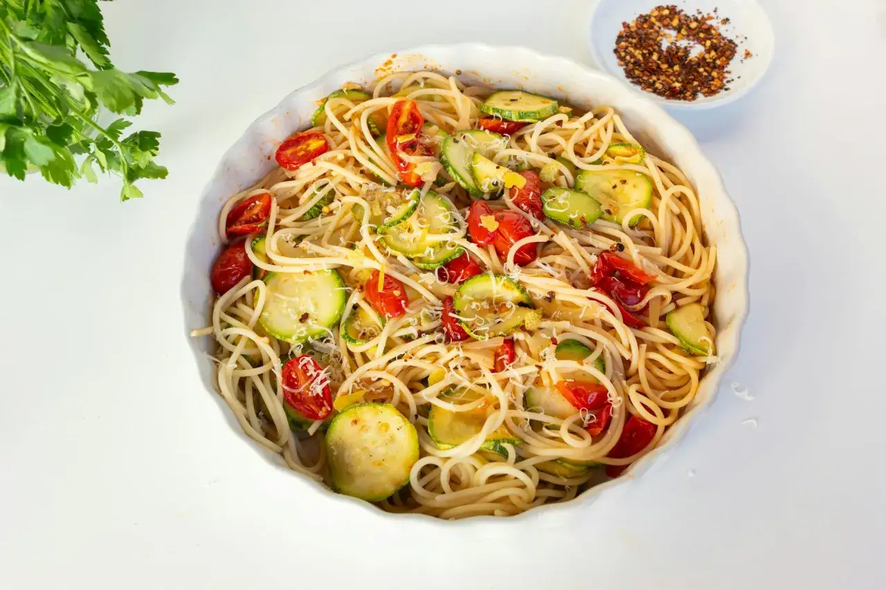 Pyszny makaron z cukinią i pomidorami, posypany parmezanem i płatkami chili.