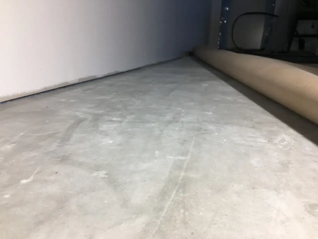 Oj&auml;mn betongyta som v&auml;ntar p&aring; att slipa betong f&ouml;r en j&auml;mn finish. En rulle skyddspapper ligger l&auml;ngs v&auml;ggen.