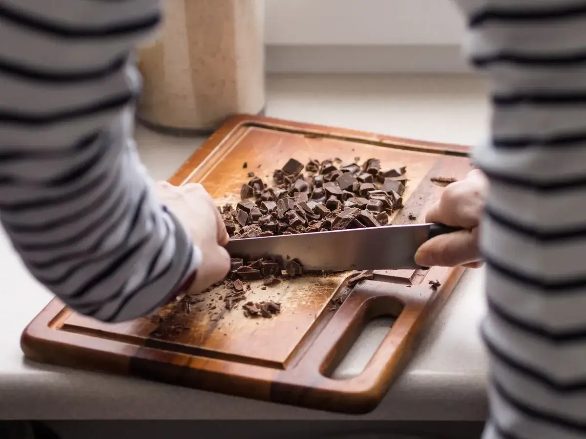 Une personne utilise un couteau pour comment casser une tablette de chocolat en pépites sur une planche à découper en bois.
