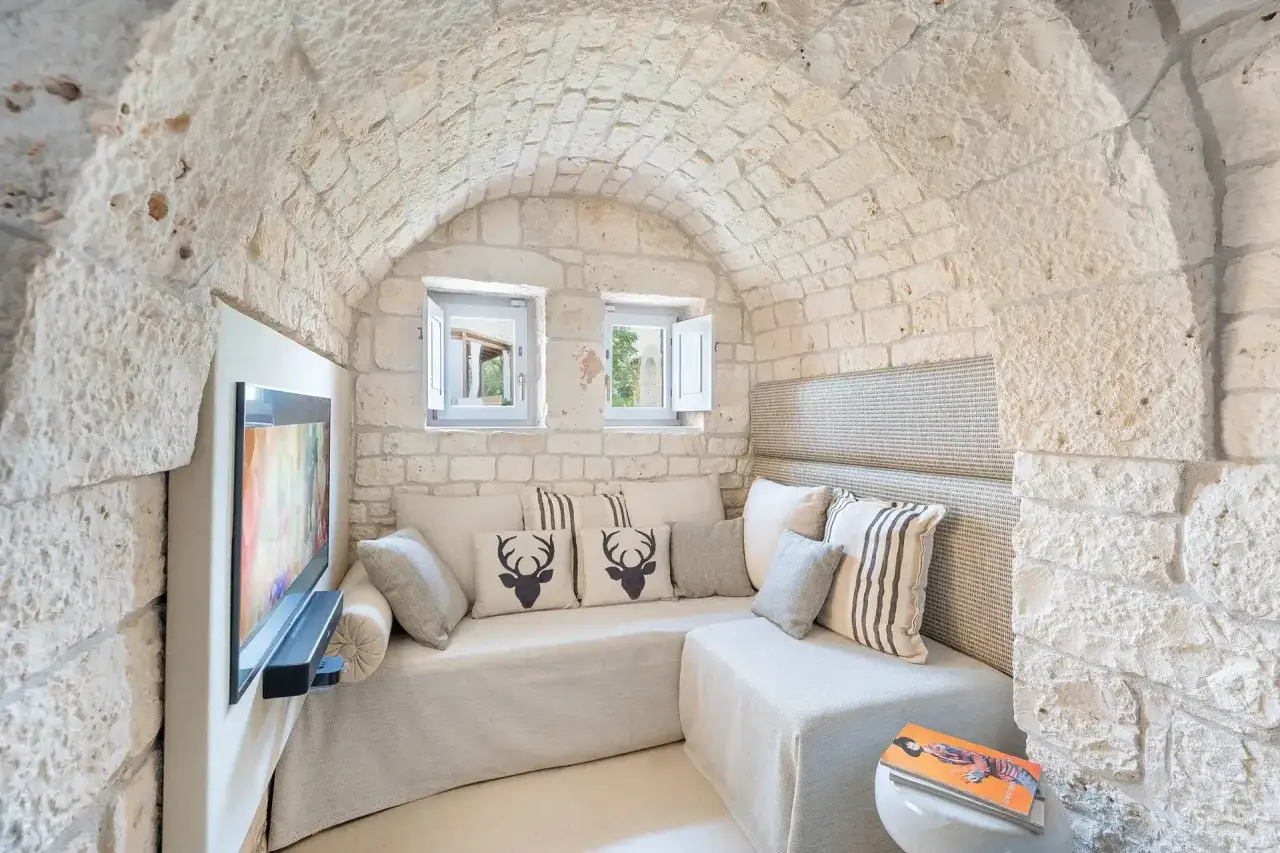 Interni di trulli puglia: divano accogliente sotto soffitto a volta in pietra, con cuscini decorativi e TV a parete.