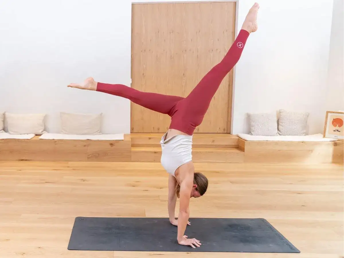Mujer en equilibrio sobre las manos en la postura de yoga Eka Pada Koundinyasana, con las piernas extendidas en direcciones opuestas.