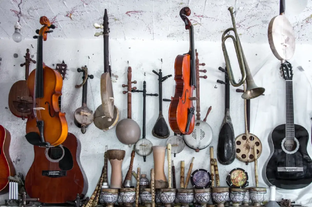 Wiele instrumentów strunowych, w tym skrzypce, gitary i tradycyjne instrumenty ludowe, wisi na ścianie.