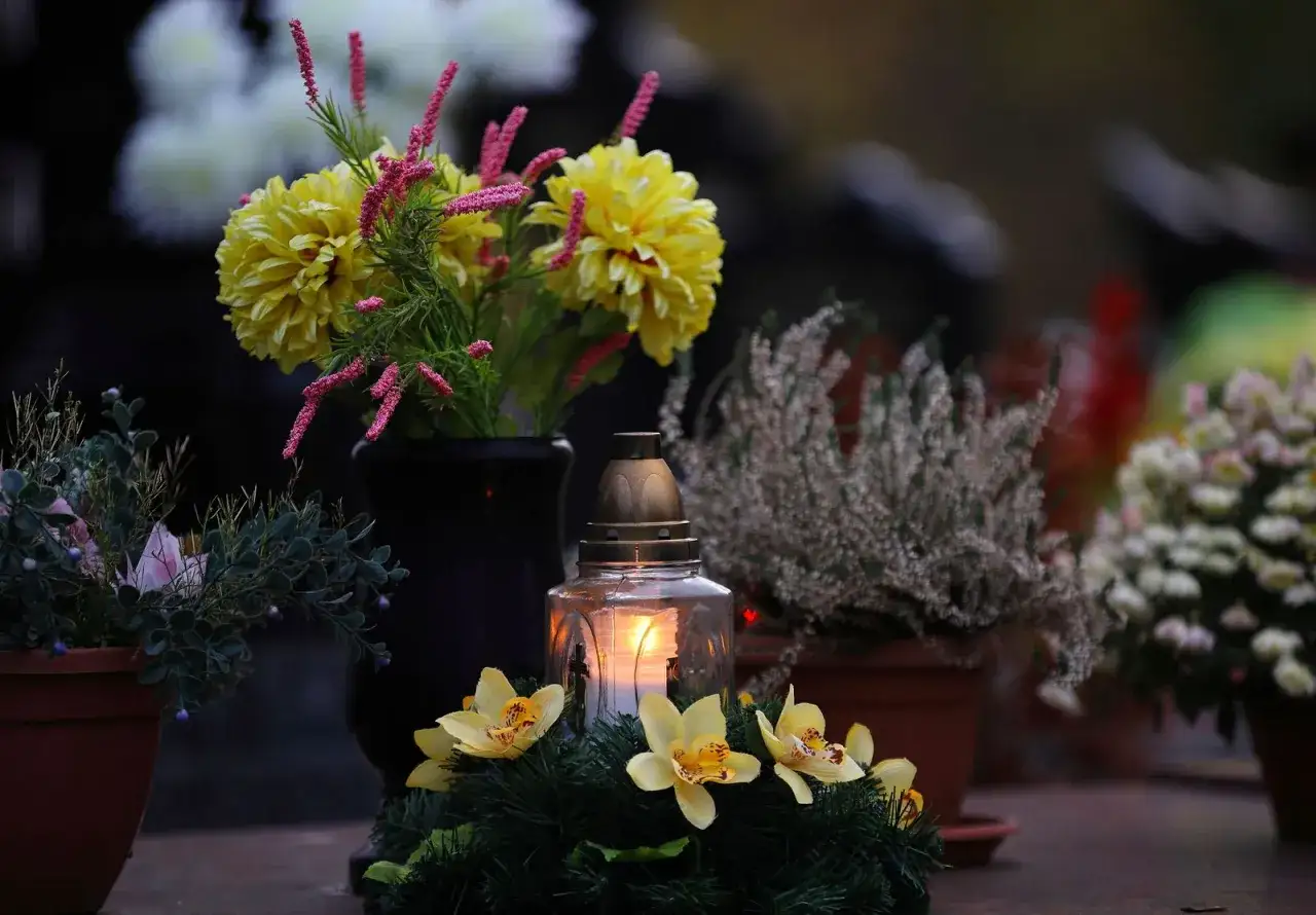 Vela encendida y flores amarillas en un cementerio, evocando el esp&iacute;ritu del 1 de noviembre y frases para el D&iacute;a de Todos los Santos.