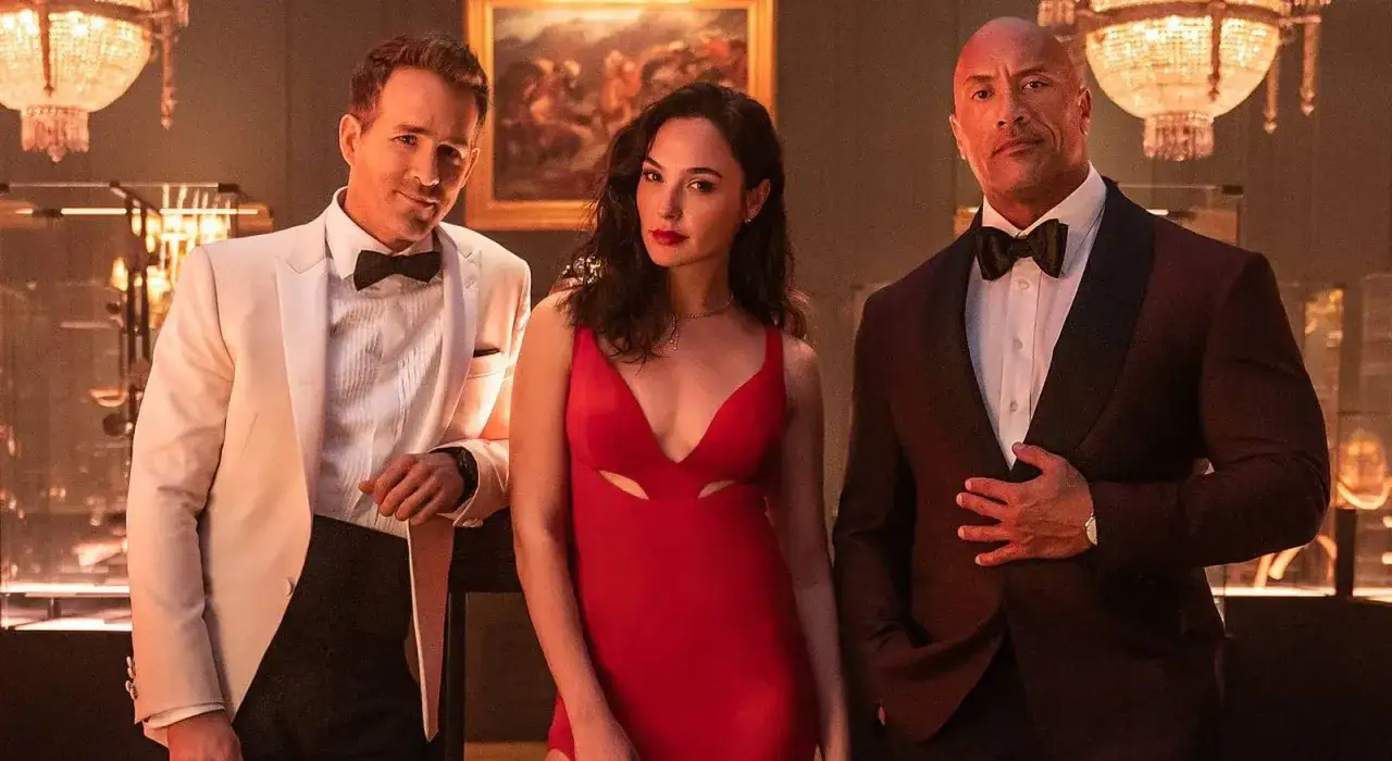Ryan Reynolds, Gal Gadot w czerwonej sukni i Dwayne Johnson w garniturze, wyglądają jakby szykowali się do akcji w filmie 