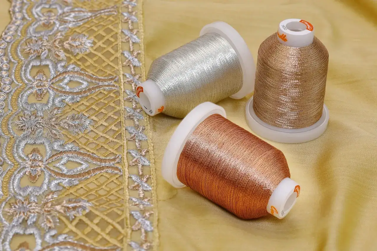 Trois bobines de fil métallique argenté, cuivre et bronze, prêtes à être utilisées dans les textiles pour créer des broderies éclatantes.