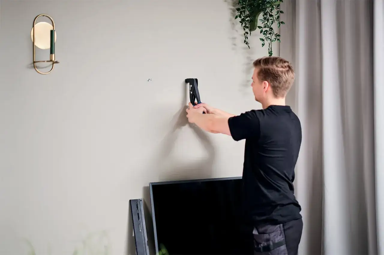 Un homme utilise un outil pour fixer un support mural, une étape clé pour fixer un meuble lourd sur placo.