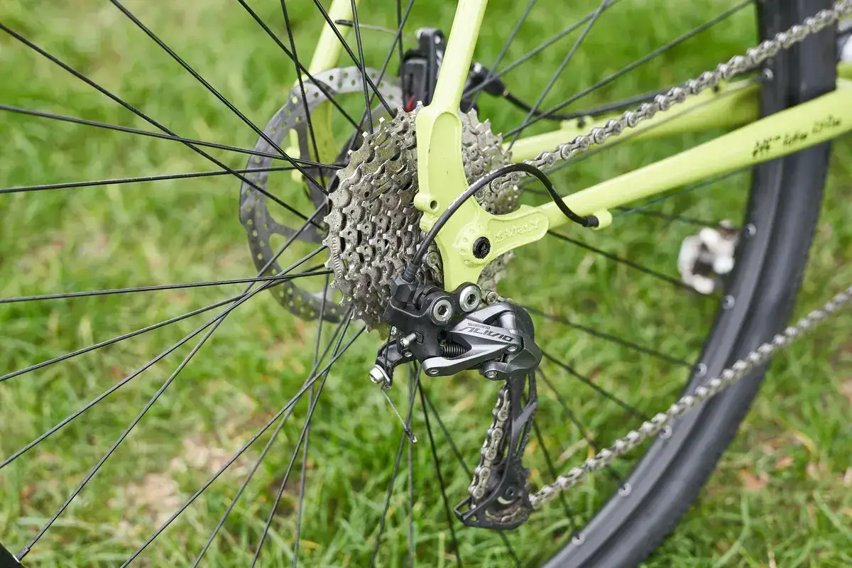 Tylna przerzutka rowerowa Shimano Alivio z widoczną długością w&oacute;zka przerzutki, zamontowana na zielonej ramie roweru Surly.