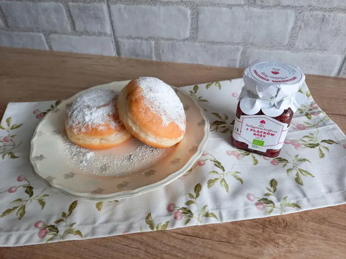 Pączki z przepisu Ewy Wachowicz, oprószone cukrem pudrem, obok słoiczka konfitury z płatków róży.