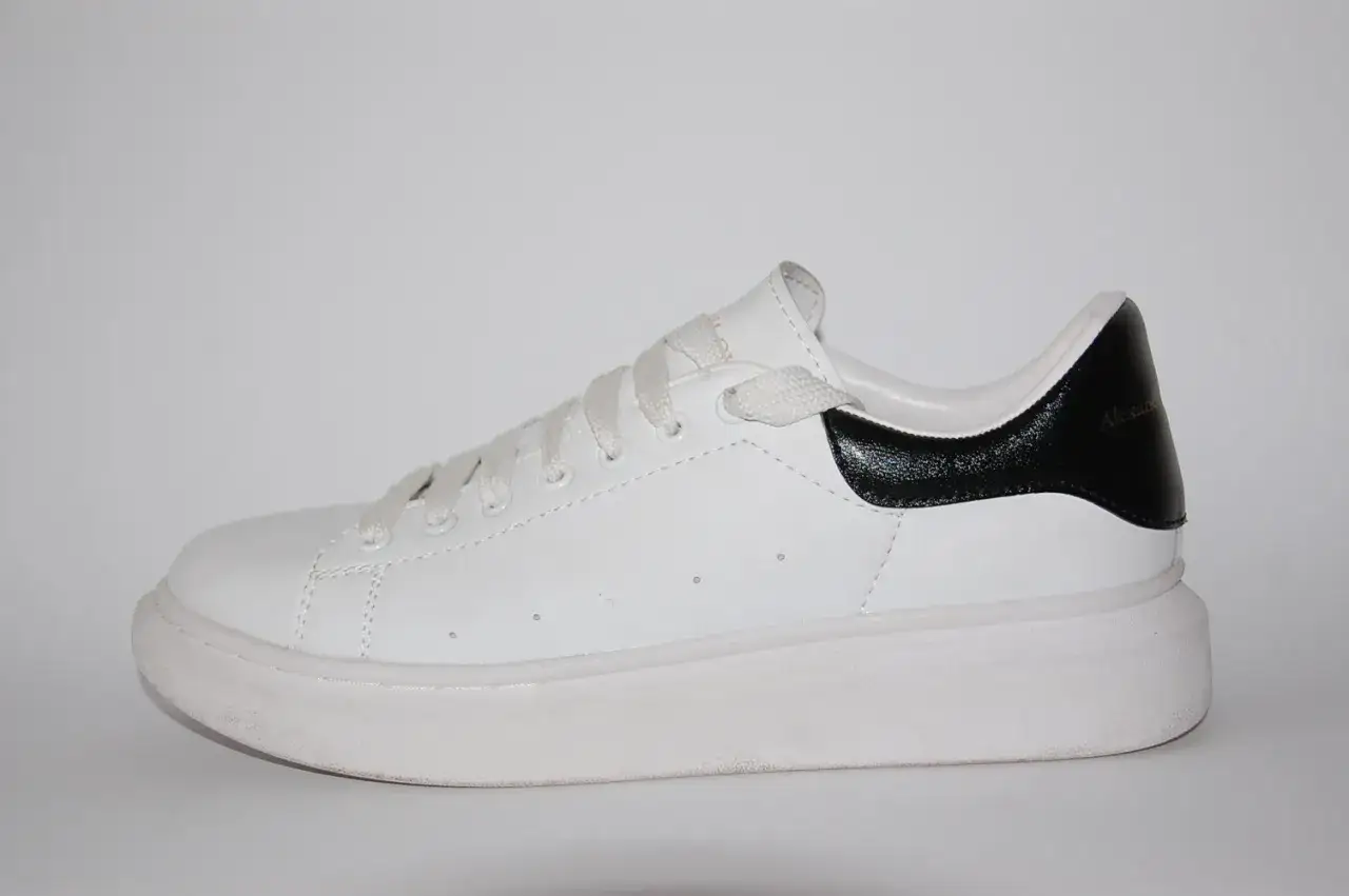 Białe sneakersy Alexander McQueen z czarną, błyszczącą piętą. Klasyczny model na grubej podeszwie.