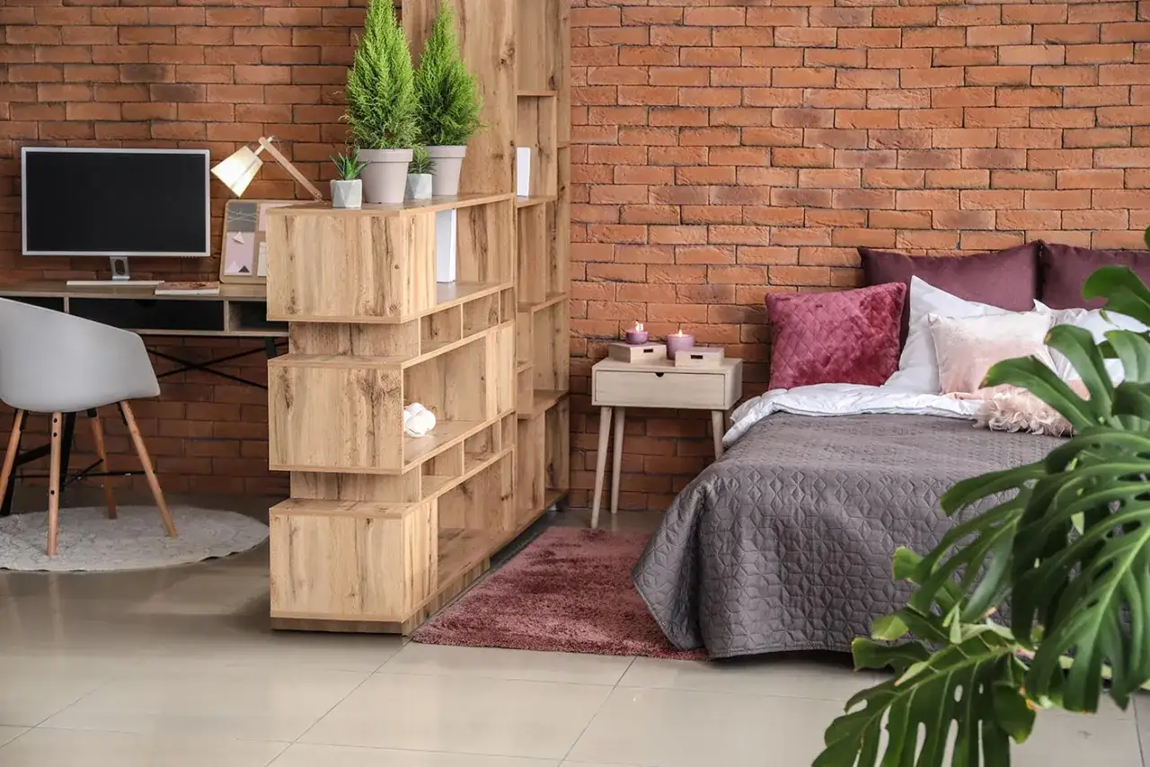 Soluzione d'arredo per come arredare un monolocale di 40 mq: letto, scrivania, libreria divisoria e piante creano uno spazio funzionale e accogliente.