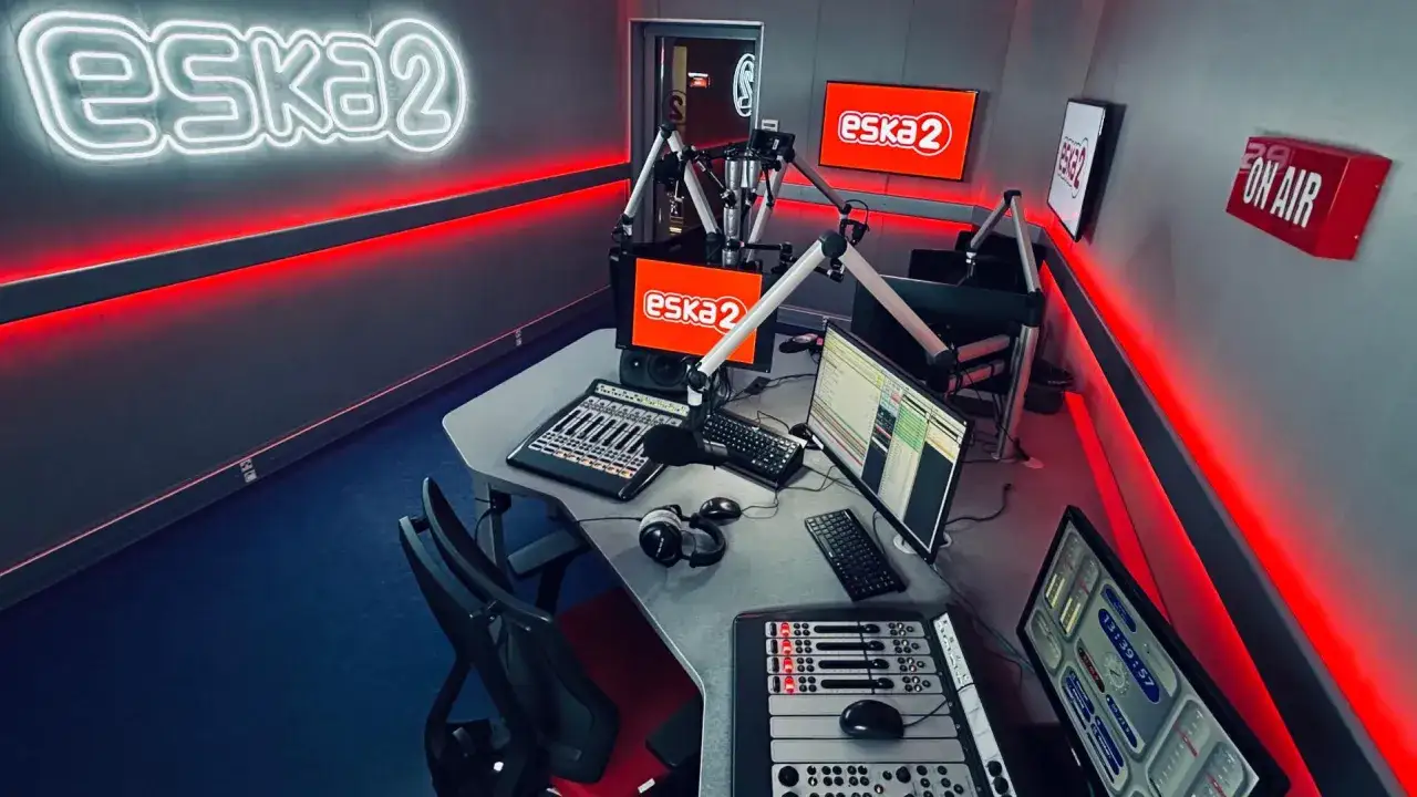 Studio radiowe Eska2 z neonowym logo, mikrofonami i konsoletami. Czerwone światła tworzą atmosferę niczym radio supernova.