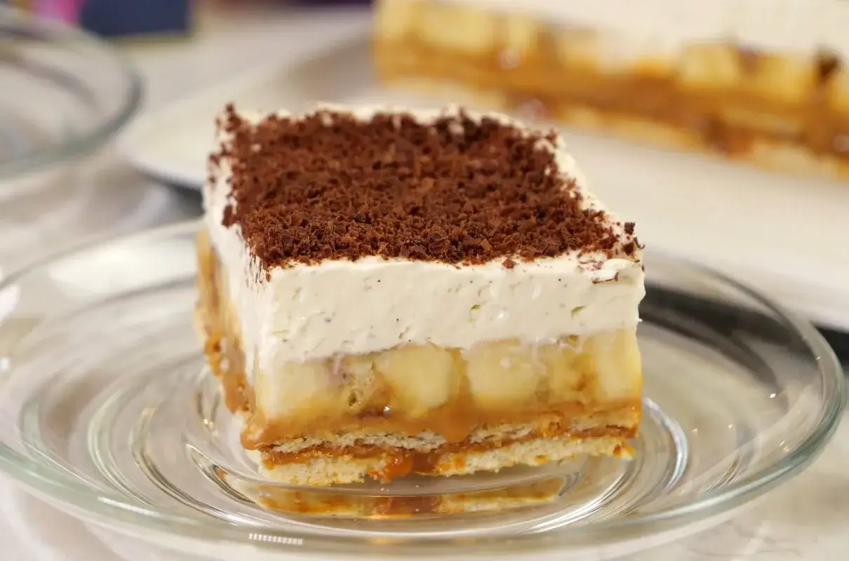 Pyszny kawałek ciasta banoffee na talerzyku. Warstwy banana, karmelu i bitej śmietany, posypane czekoladą. Idealny banoffee przepis.