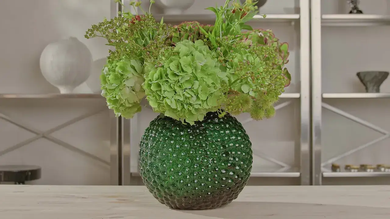 En grön, bubblig vas med en bukett av krysantemum snittblomma och andra gröna blommor.