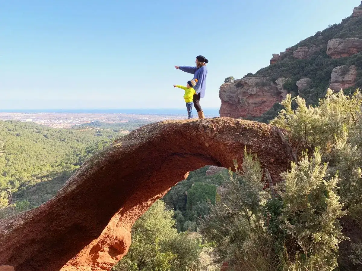 Madre e hijo se&ntilde;alan el horizonte desde un arco de roca, con vistas a la costa y a los planos cerca de Barcelona.