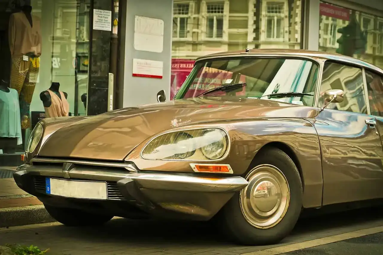 Brązowy, zabytkowy Citroen DS, jeden z kultowych **citroen modele stare**, zaparkowany przed sklepem z odzieżą.