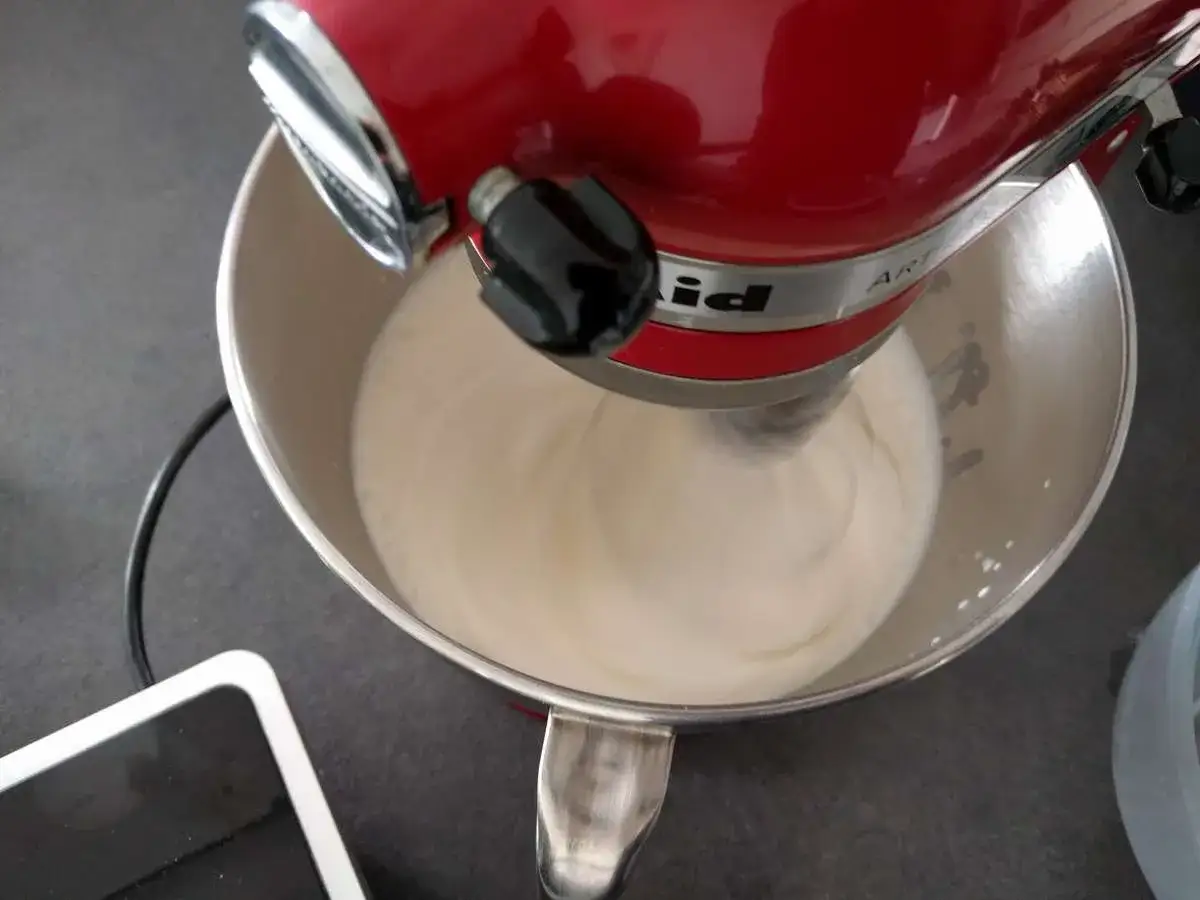 Un robot pâtissier rouge mélange une crème onctueuse, étape clé pour une délicieuse pâte à bombe.