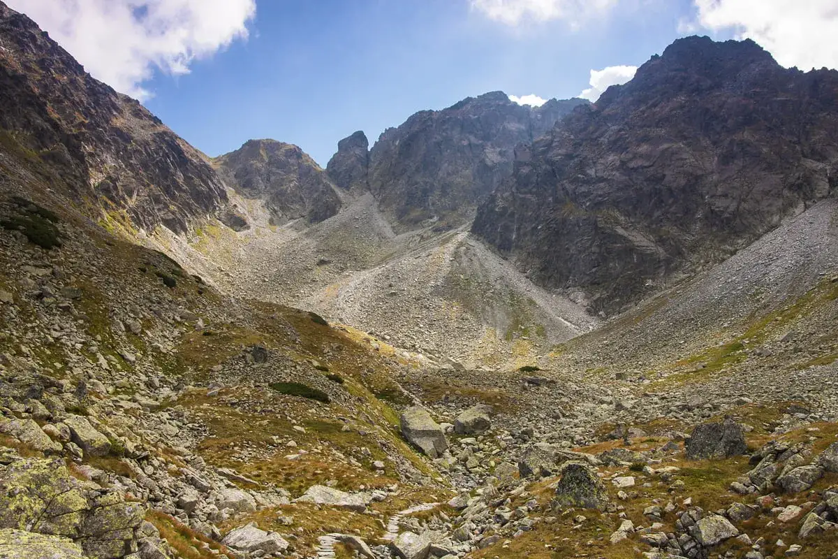 Kamienista dolina w górach, skaliste zbocza, trawy i chmury na niebie. Widok na krzyżne.