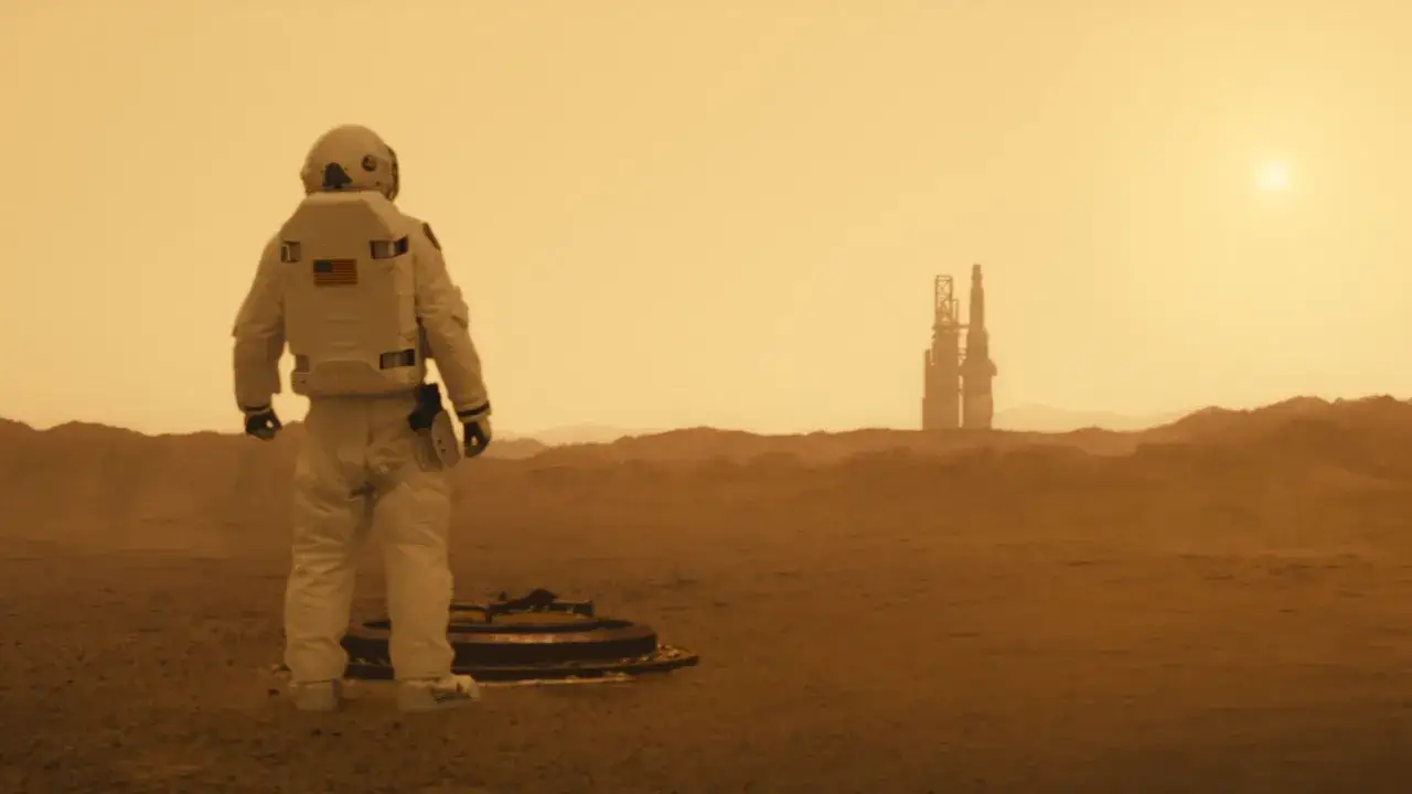 En astronaut står på Mars, med en farkost vid sina fötter. I fjärran syns en byggnad. En scen från Ad Astra, en film som förtjänar en recension.