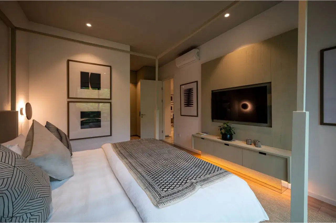 Acogedora habitación pequeña con cama, cuadros abstractos, TV y luz ambiental cálida.