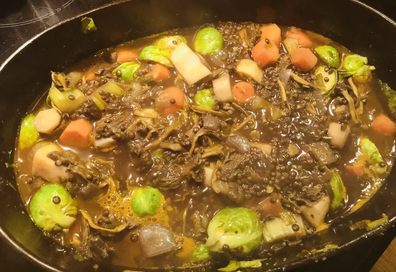 En mustig vegetarisk gryta med linser, brysselk&aring;l, mor&ouml;tter och rotfrukter som puttrar i en kastrull.